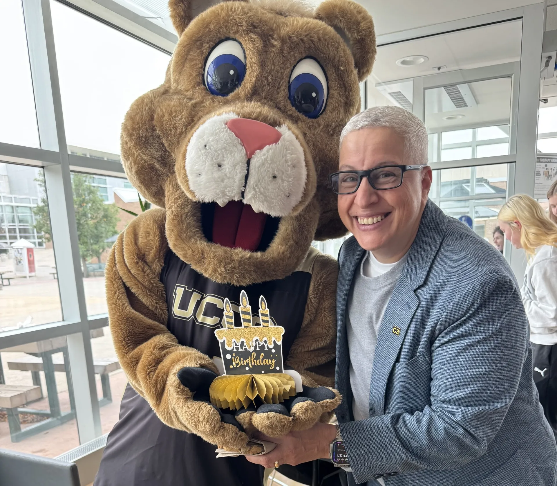 Provost Lynn Vidler and UCCS mascot Clyde hold a birthday cake for their shared birthday